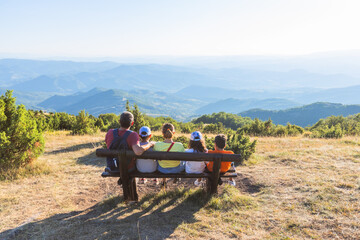 Obraz premium Group of friends enjoying mountain view from wooden bench viewpoint