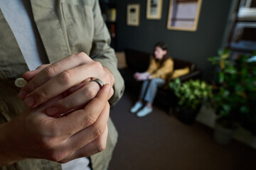 Caucasian young adult man removing wedding ring with blurred Caucasian young adult woman sitting on...