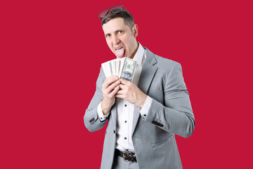 A man in a gray jacket and white shirt holds a $100 bill with his tongue hanging out. He has...