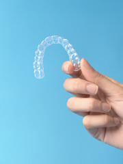 Clear aligner in womans hand on blue background for teeth straightening