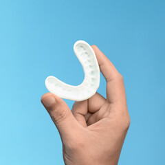 Closeup of a hand holding a white dental mouth guard on blue background