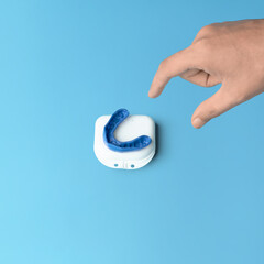 Hand reaching for a blue dental mouth guard in a case on blue background