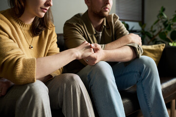 Caucasian young adult woman and Caucasian young adult man sitting close together on sofa holding...