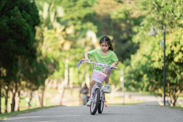 Naklejka premium Young girl riding bicycle in park during sunny day, enjoying outdoor adventure, cheerful expression, childhood joy, playful moments, vibrant greenery