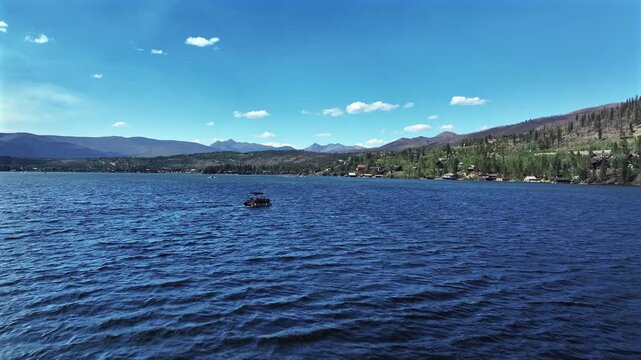 Summer pontoon yacht boating at Grand Lake Granby aerial drone Colorado Rocky Mountains National Park entrance breeze on body of water sunny morning daytime clouds lake homes forward motion