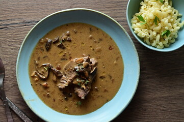 Top view of a traditional Czech dish — beef with mushrooms — served on a blue plate. A...