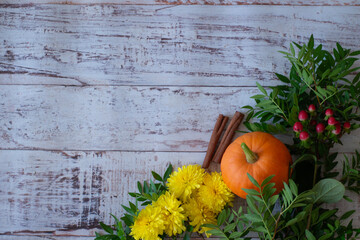 Autumn bright colored background for text, a composition of pumpkins, yellow flowers, and green branches on a wooden table