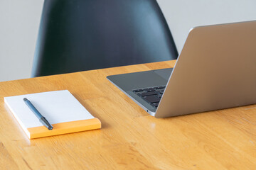 ノートパソコンとメモ帳が置かれた木製デスクのワークスペース