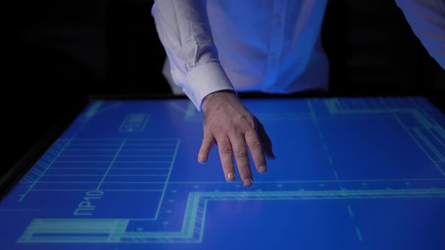 In office on big touch screen like a desk, man moving blue print by his hand 