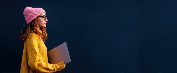 The trendy woman holding a laptop against a blue background.