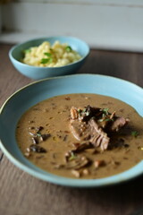 Daily menu with a traditional autumn dish — beef with mushroom sauce served on a blue plate. A hearty Czech-style meal with tender beef, pasta, and mushrooms, presented in a rustic homemade style