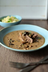 Daily menu with a traditional autumn dish — beef with mushroom sauce served on a blue plate. A hearty Czech-style meal with tender beef, pasta, and mushrooms, presented in a rustic homemade style
