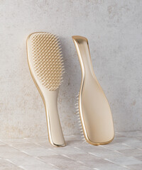 Two gold and beige hairbrushes leaning against tiled wall