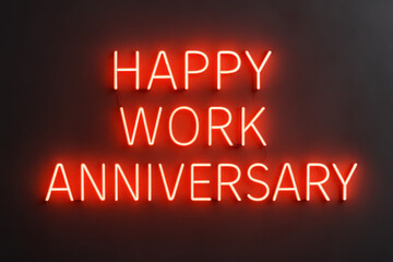 Happy work anniversary neon sign glows with cheerful red light on dark wall creating festive and modern atmosphere for celebrating workplace milestones