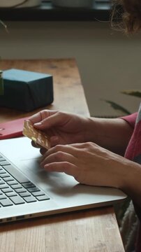 Vertical video. Woman shopping online for Christmas, sitting at desk, using payment card and laptop