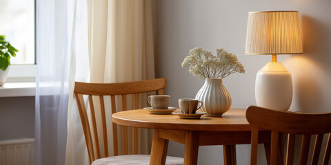 Cozy corner dining space with wooden table, two chairs, ceramic cups, vase with flowers, and warm lamp light