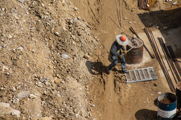Worker Handling Steel Rods at Construction Site with Soil Background
