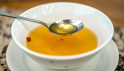 Golden liquid in a white bowl, spoon lifting a sample, close-up view.