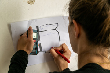 Close-up of female architect drawing on house blueprints with pen during construction. Electronic...