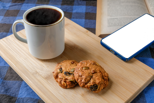 Relaxing top view of black coffee in a white ceramic mug with homemade cookies on a wooden cutting board, placed beside a smartphone and an open book. Perfect for lifestyle, cafe, and digital design - Powered by Adobe