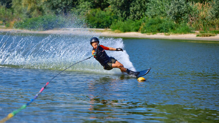 Young boy in black helmet making powerful water skiing turn with spray. Concept of youth...