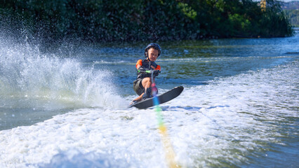 Boy in black helmet leaning forward while water skiing with splash trail. Concept of balance,...