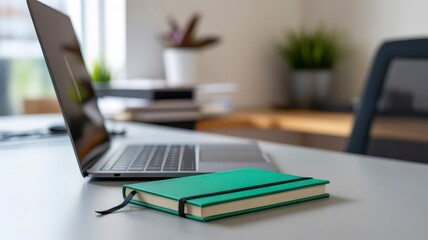 Workspace with Notebook Laptop and Green Journal on White Table with Office Background