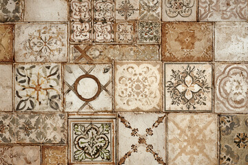 A collection of square tiles with various floral and geometric patterns in muted beige and brown tones creating a rustic vintage design