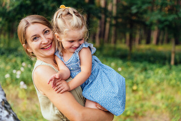 Mother holding little daughter outdoors in forest authentic family lifestyle