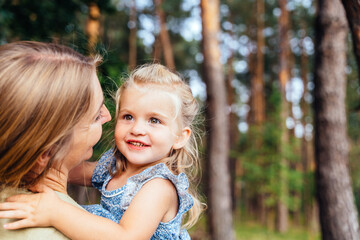 Mother holding daughter outdoors in forest looking at each other with smile