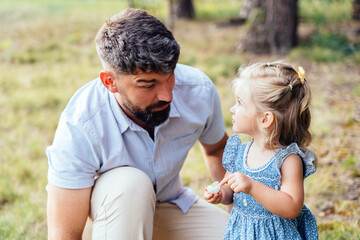 Father looking at daughter outdoors in forest holding shell authentic family lifestyle