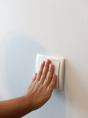 Child hand pressing light switch on white wall in modern room, kid turning on light