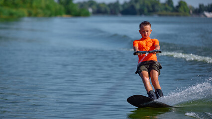 Boy wakeboarding smoothly on calm lake with serious concentration. Concept of mindfulness, balance,...