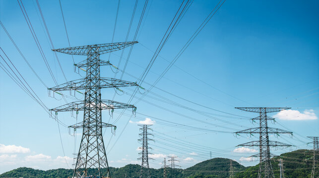 High voltage electricity transmission pylons and power lines crossing over green hills under a clear blue sky on a sunny day.