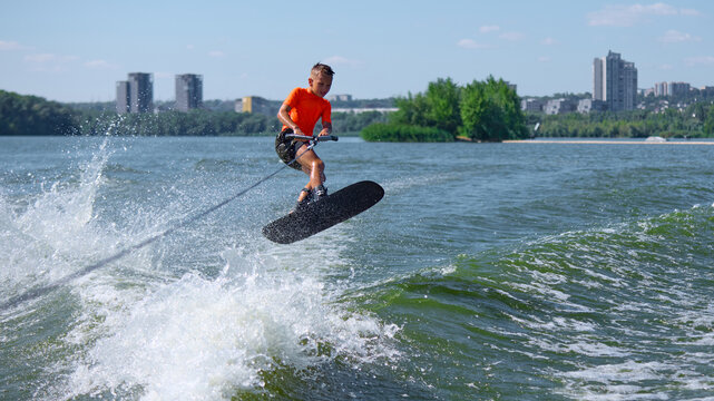 Boy wakeboarder airborne trick over river waves with confident focus. Concept of athletic training, passion, youthful energy, motion, and extreme water sport lifestyle.