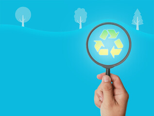 Hand holding magnifying glass, focus on recycling icon
