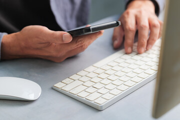 Man checking information with smartphone and keyboard simultaneously