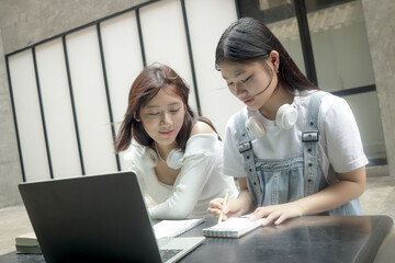Two Asian teenage girls studying together. High school young women using laptop computer and documents paper to study. Female teenager students consulting for school assignment and doing homework.