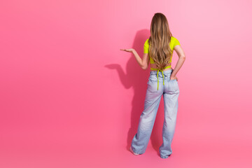 Cheerful blonde woman in a stylish yellow top posing with a charming hand gesture against a vibrant pink background