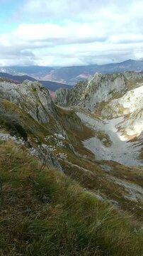 Standing high on a slope on a trail, a man enjoys a scenic view of the mountains and valley on an autumn day. Route to &Scaron;uplja vrata in Prokletije National Park, Montenegro. Hiking in the Dinaric Alps