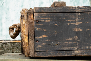 An old wooden box with worn black paint and rusty nails, with a rope handle visible on the side on...