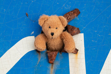 A damaged blue road sign with a large hole and a teddy bear sticking out of it during shelling