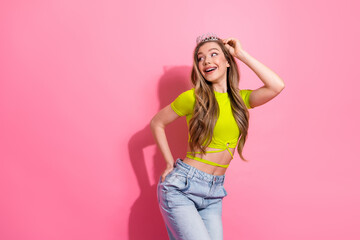 Cheerful young woman wearing a crown on her head against a pink background celebrating happiness...