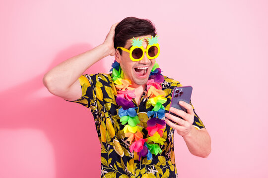 Enthusiastic young man with tropical outfit and phone celebrating against vibrant pink background