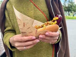 Juicy delicious hot dog in the hands of a girl on a warm day. High quality photo
