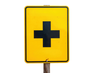Yellow road sign with a bold black cross indicating an intersection, mounted on a wooden post.