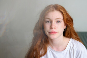 Relaxed teenager with long auburn hair and minimal makeup in a cozy indoor setting.