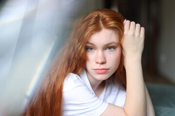 Fototapeta premium Portrait of a young girl with long red hair and green eyes in natural light, wearing a white t shirt.