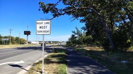 An American highway with a sign indicating movement and a right turn, an empty highway during the day with information signs and an electronic board, road markings and signs indicating the direction