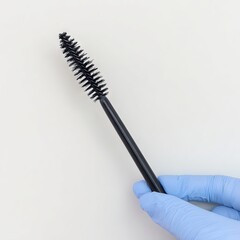 Black mascara wand held by gloved hand against a clean white background, showcasing beauty product details and emphasizing cosmetic application techniques for makeup enthusiasts
